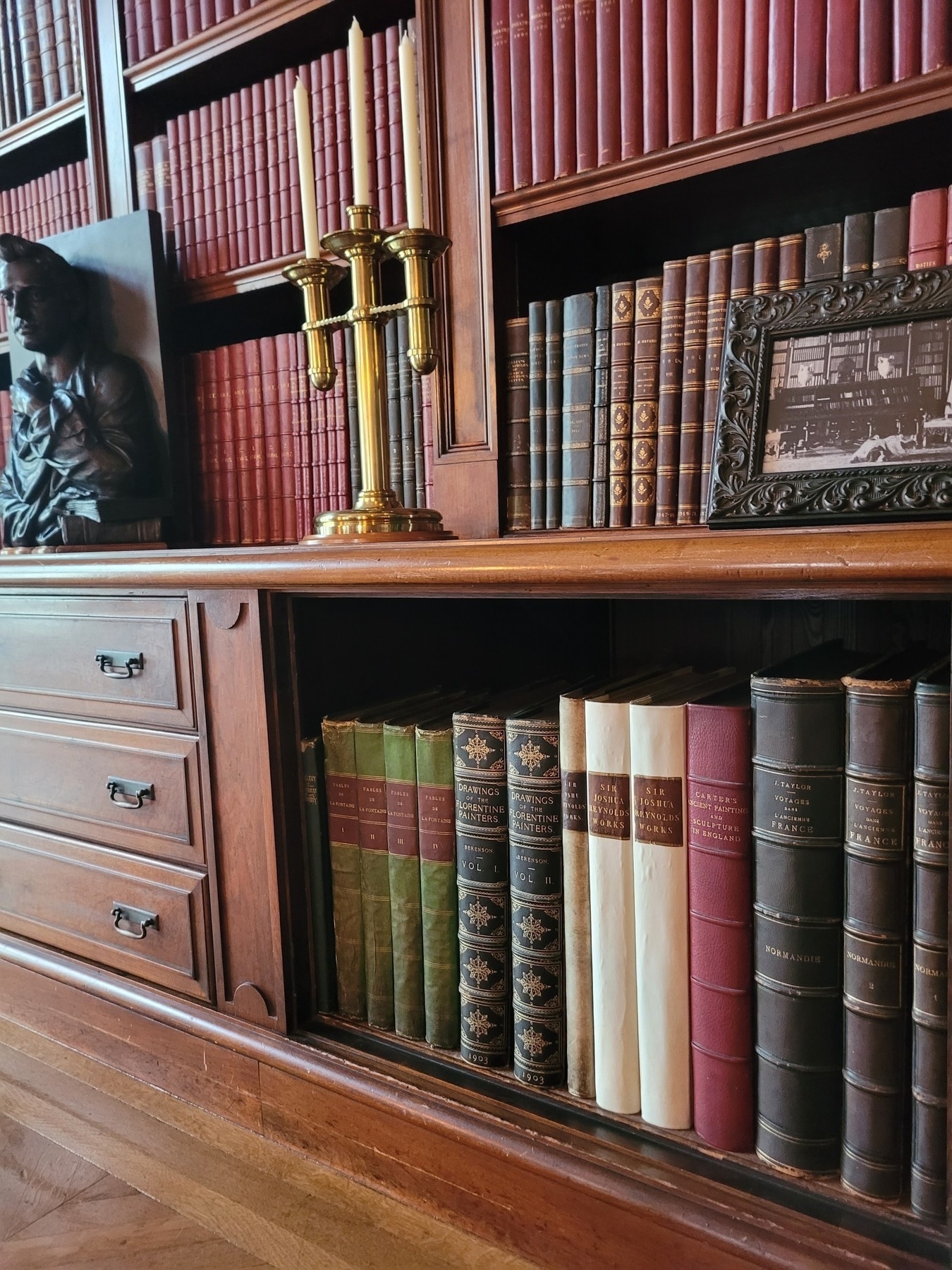 Auto-generated description: A wooden bookshelf filled with vintage books is adorned with a brass candelabra and decorative items.